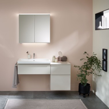 Umywalka z meblami łazienkowymi, umywalką i szafką lustrzaną Geberit na tle pastelowej ściany