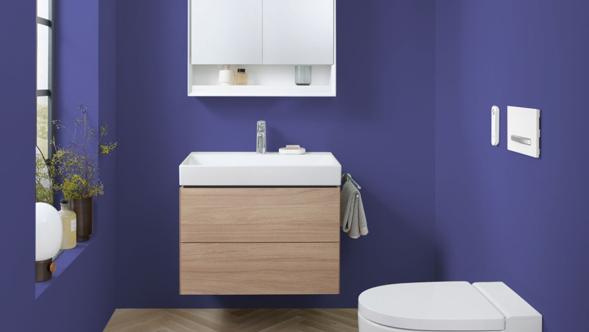 Bagno con ceramiche e mobili da bagno Geberit davanti a una parete dipinta con il colore di tendenza 2022 «Very Peri».