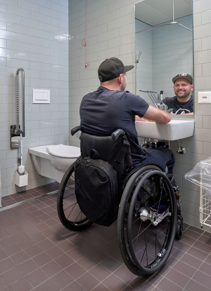 Peter Roos sulla sua sedia rotelle nella zona lavabo di un bagno senza barriere (© Ben Huggler) 